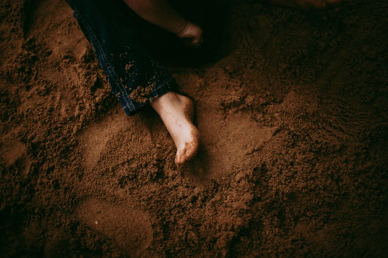 a close up of a person's feet in the sand, an album cover, trending on pexels, brown mud, dark, childish, cinnamon skin color