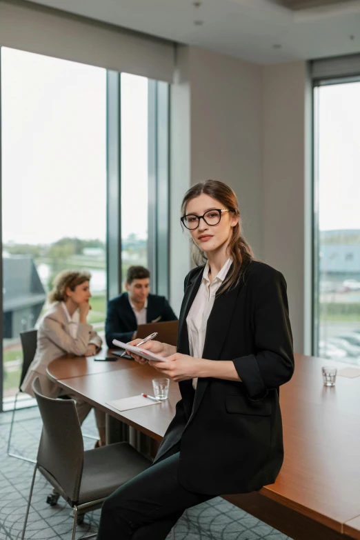 a woman sitting at a table in front of a group of people, in a business suit, high-quality photo, trending artstayion, looking confident