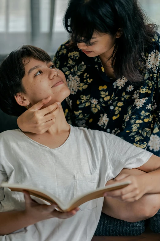 a man sitting on a couch next to a woman reading a book, trending on pexels, portrait of 14 years old boy, arm around her neck, boy has short black hair, supportive