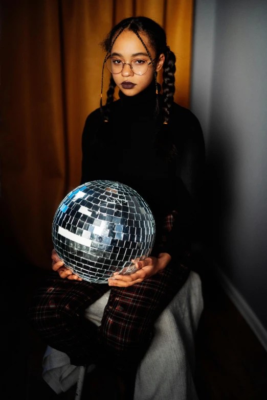 a woman holding a disco ball in her hands, an album cover, by Julia Pishtar, trending on pexels, afrofuturism, girl with glasses, box braids, ((portrait)), indoor picture