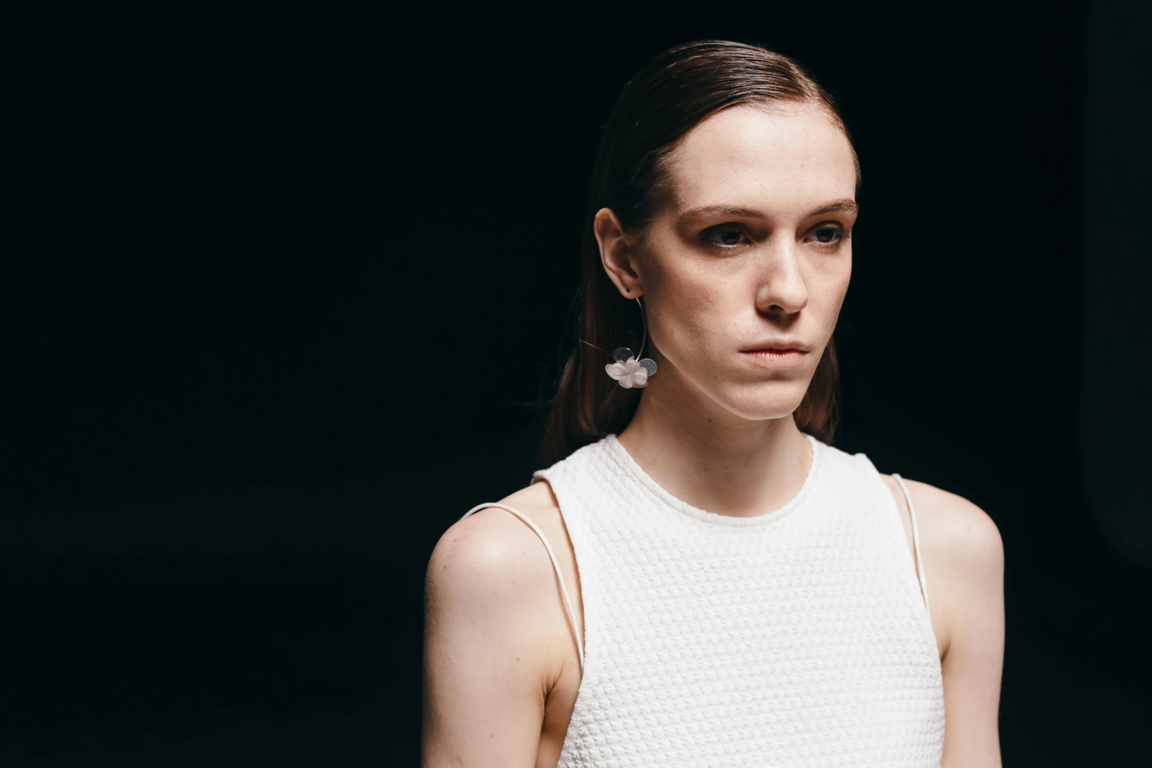 a woman standing in front of a black background, by Nina Hamnett, trending on unsplash, bauhaus, fashion week backstage, wearing pearl earrings, off - white collection, sydney hanson