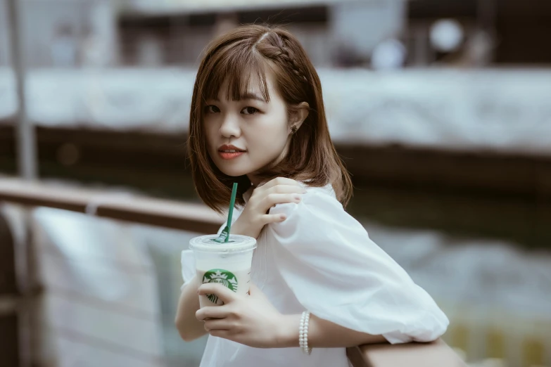 a woman standing next to a railing holding a drink, inspired by Tan Ting-pho, trending on pexels, young cute wan asian face, starbucks, dressed in white, halfbody headshot