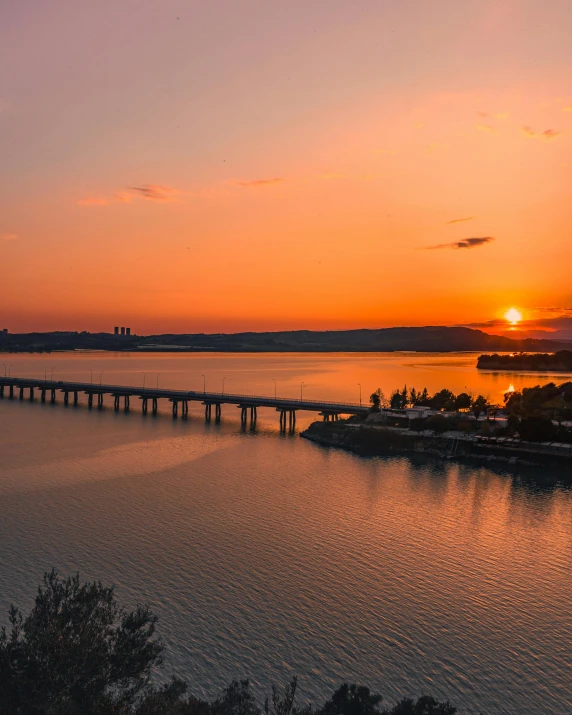 the sun is setting over a large body of water, pexels contest winner, rostov city, city bay bridge aqueduct, beautiful lake in the foreground, overlooking