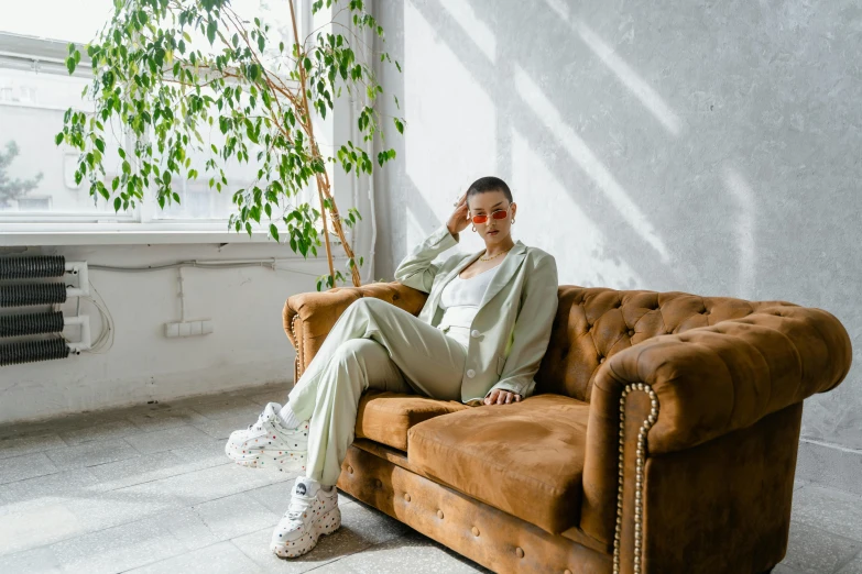 a woman sitting on top of a brown couch, by Emma Andijewska, trending on pexels, wearing fashion suit, pastel green, wearing white sneakers, queer woman