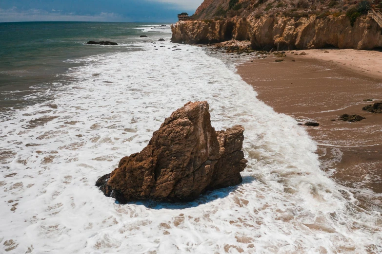 a large rock sitting on top of a sandy beach, unsplash, renaissance, malibu canyon, waves crashing in the sea, realistic »