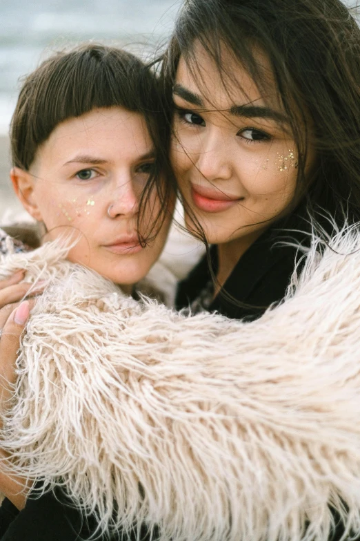 two women hugging each other on the beach, an album cover, by Attila Meszlenyi, trending on pexels, fur jacket, headshot, mai anh tran, nonbinary model