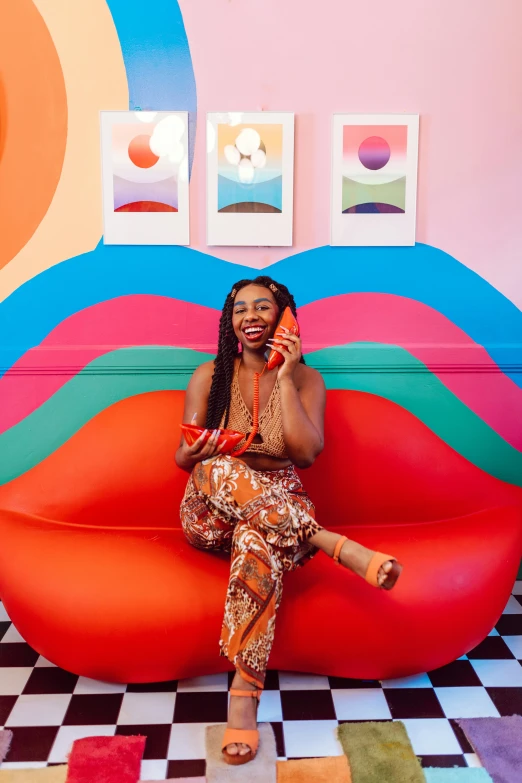 a woman sitting on a couch talking on a cell phone, maximalism, vanessa blue, verner panton, bright colors with red hues, open happy mouth