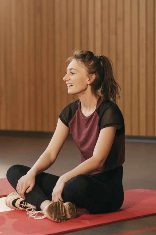 a woman sitting on top of a red mat, inspired by Elizabeth Polunin, trending on pexels, smiling young woman, looking left, in a gym, digital still