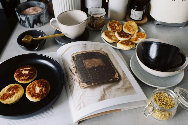 a table topped with plates of food and a book, a still life, unsplash, private press, pancakes, dwell, old photobook, background image