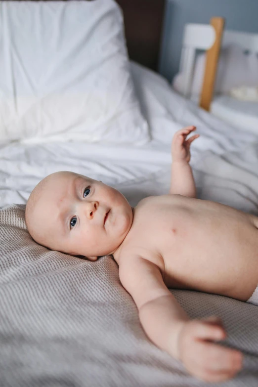 a baby in a diaper laying on a bed, by Jaakko Mattila, pexels contest winner, detailed skin, bumps, confident looking, looking across the shoulder