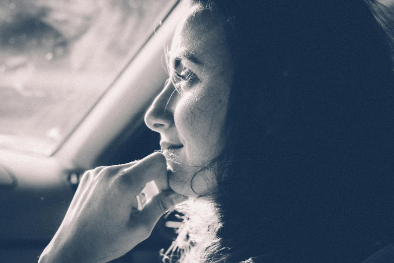 a woman sitting in a car talking on a cell phone, a black and white photo, pexels contest winner, romanticism, window light, profile image, distant thoughtful look, woman with black hair