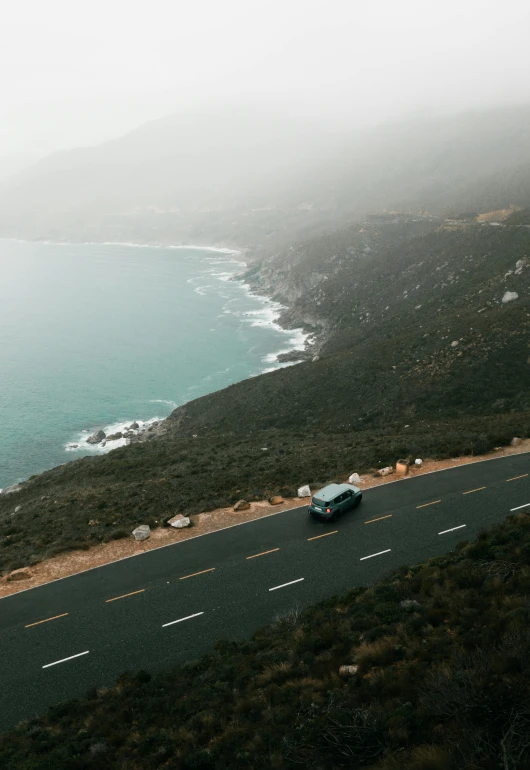 a car driving down a road next to the ocean, by Lucas Vorsterman, unsplash contest winner, large cape, teal color graded, hills and ocean, multiple layers