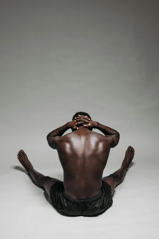 a man sitting on the ground with his hands on his head, black arts movement, muscular bodies, backfacing, rankin, chocolate