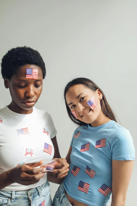 a couple of women standing next to each other, a portrait, trending on unsplash, american romanticism, gang flags, body paint, leslie zhang, wearing shirts