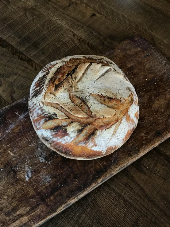 a loaf of bread sitting on top of a wooden cutting board, andrew bernstein, woodfired, covered in white flour, detailed product image