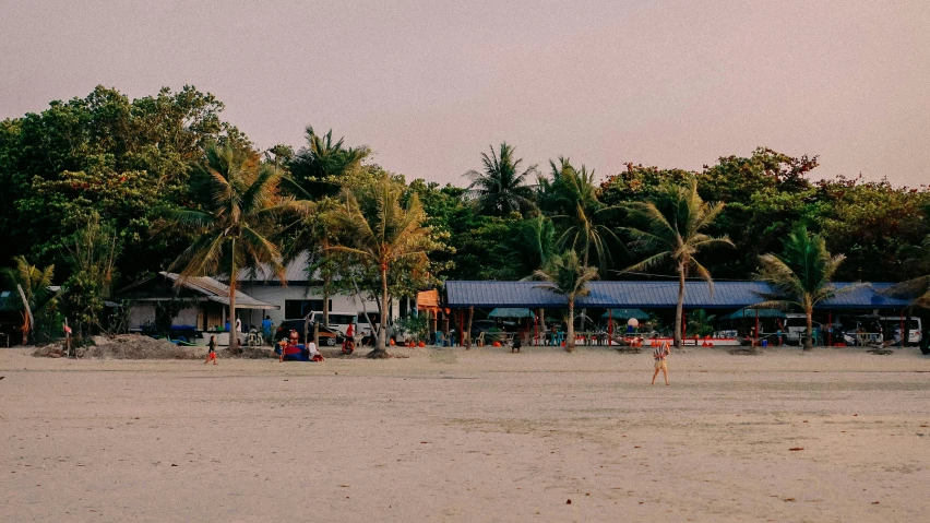a group of people standing on top of a sandy beach, coconut trees, bangkok, huts, during golden hour