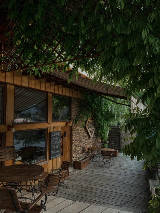 a patio with tables and chairs under a tree, a portrait, by Kristian Zahrtmann, unsplash, polygonal wooden walls, low quality photo, covered in vines, storefront