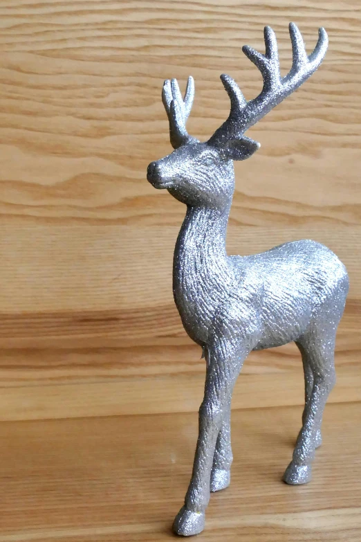a silver deer figurine sitting on top of a wooden table, tall shot, aluminum sheen, ultra textured, very crisp
