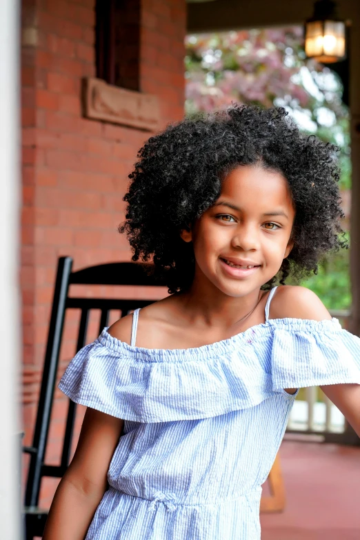 a young girl in a blue dress standing on a porch, a portrait, by Lily Delissa Joseph, pexels, black curly hair, official screenshot, portrait n - 9, sunlit