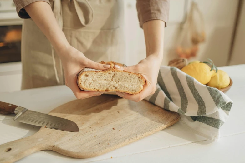 a person holding a loaf of bread on a cutting board, a picture, inspired by Richmond Barthé, pexels contest winner, press shot, covered, at home, linen