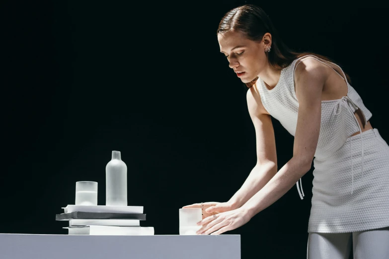 a woman standing in front of a stack of books, a marble sculpture, inspired by Vanessa Beecroft, unsplash, minimalism, flasks in hands, sitting on a lab table, pouring, issey miyake