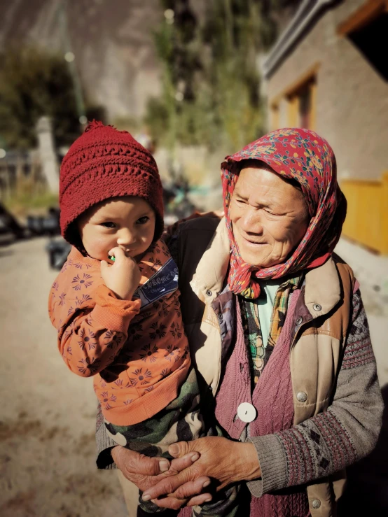 a woman holding a child in her arms, inspired by Steve McCurry, pexels contest winner, omar shanti himalaya tibet, elderly, taken on iphone 14 pro, with village