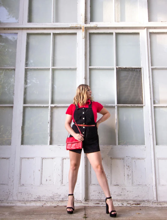 a woman standing in front of a white door, an album cover, by Julia Pishtar, unsplash, black shirt with red suspenders, wearing shorts and t shirt, red uniform, wearing overalls