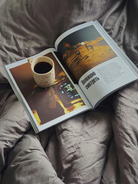 a book sitting on top of a bed next to a cup of coffee, inspired by Elsa Bleda, print on magazine, maxim shirkov, soft vinyl, full page periodical image