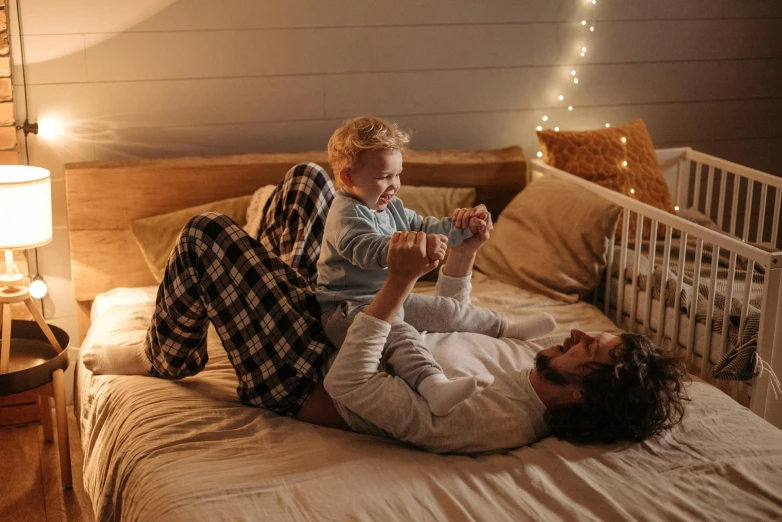 a man laying on top of a bed next to a baby, pexels contest winner, cozy lights, happy kid, gif, uk