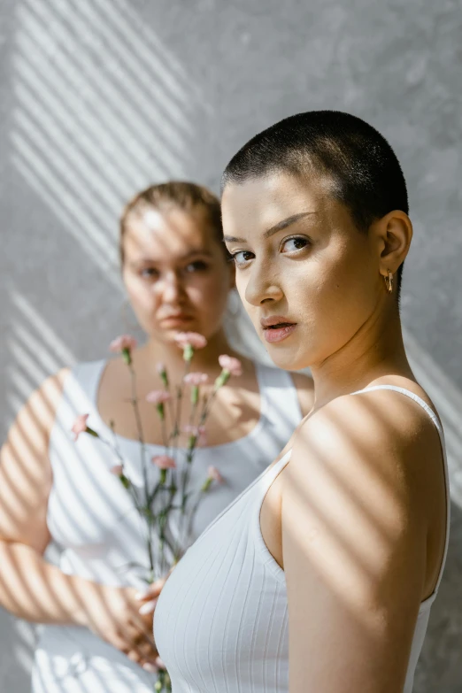 a couple of women standing next to each other, inspired by Elsa Bleda, trending on pexels, minimalism, buzz cut, sunlights, blooming, looking serious