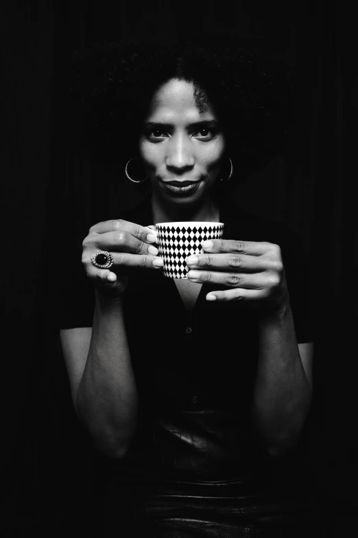 a black and white photo of a woman holding a cup, inspired by Carrie Mae Weems, annie stegg gerard, square, black main color, afro