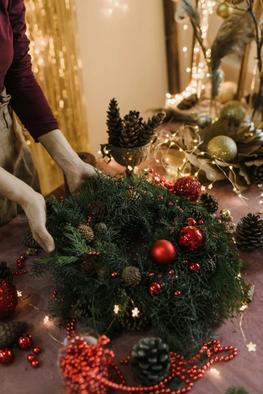 a woman decorating a christmas wreath on a table, by Julia Pishtar, intricate details. front on, fresh, uplit, contain