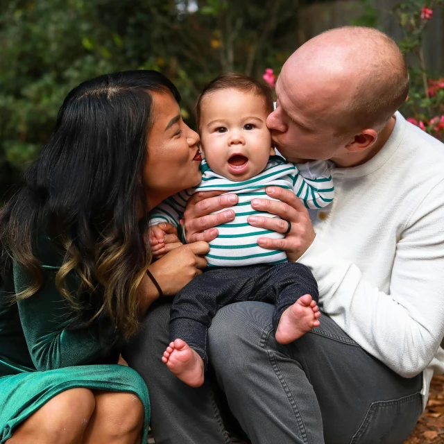 a man sitting next to a woman holding a baby, a portrait, by Carey Morris, pexels, kissing together cutely, ruan jia and greg rutkowski, bald, profile image