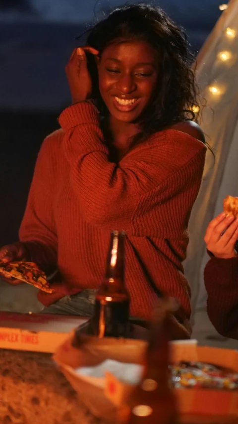 a group of people sitting around a campfire eating pizza, photo of a black woman, holiday vibe, he is wearing a brown sweater, profile image