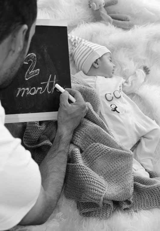 a man sitting on top of a bed next to a baby, a black and white photo, pexels contest winner, symbolism, countdown, sketching, promo image, close up details