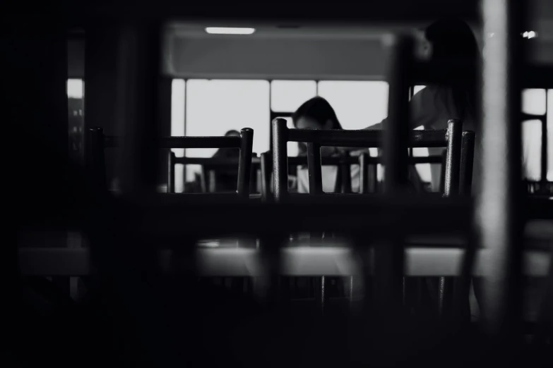 a black and white photo of a person sitting at a table, pexels contest winner, gloomy library, animation, at college, hiding