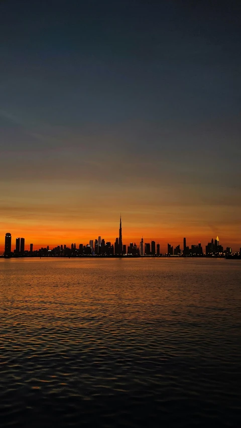 a large body of water with a city in the background, by Jacob Burck, pexels contest winner, hurufiyya, real sunset, dubai, low quality photo, new jersey