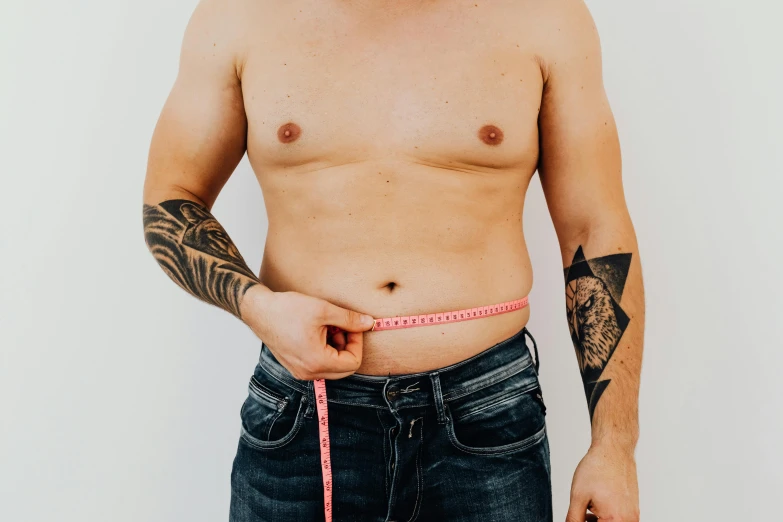 a man measuring his waist with a tape, a tattoo, by Nicolette Macnamara, trending on pexels, plain background, flat chest, lachlan bailey, belly exposed