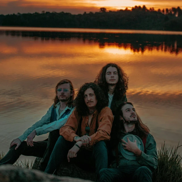 a group of people sitting next to a body of water, an album cover, pexels contest winner, antipodeans, curls, stark sunrise lighting, portrait pose, stoner rock concert