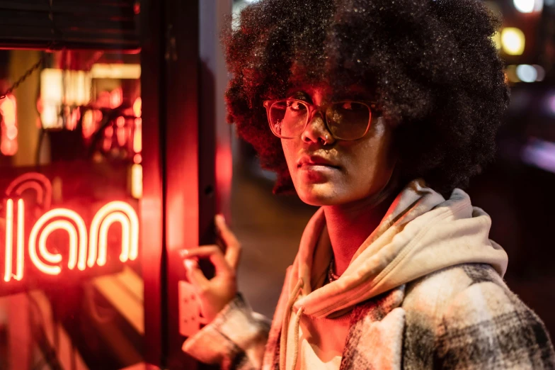 a woman standing in front of a neon sign, trending on unsplash, afrofuturism, mysterious coffee shop girl, androgynous person, with brown skin, red neon