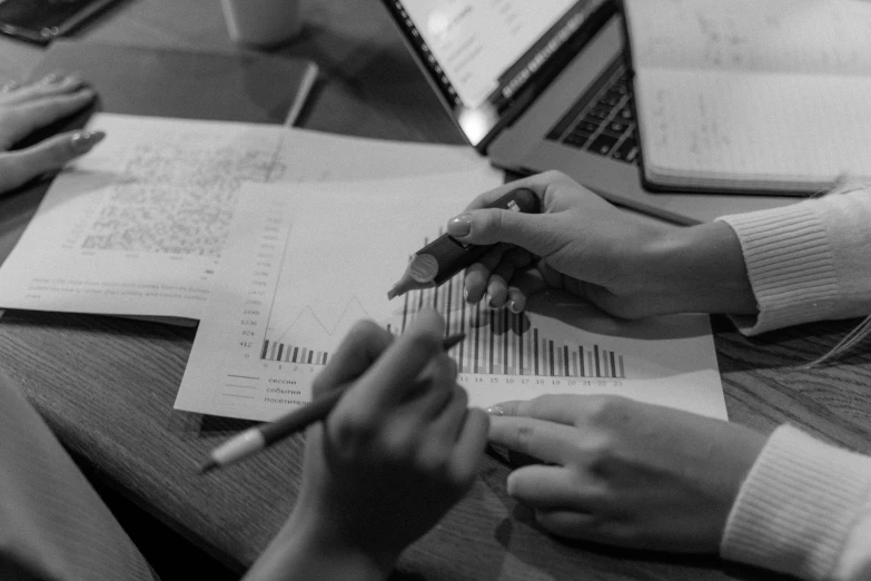 a couple of people that are sitting at a table, a black and white photo, analytical art, displaying stock charts, holding pencil, promo image, inspect in inventory image