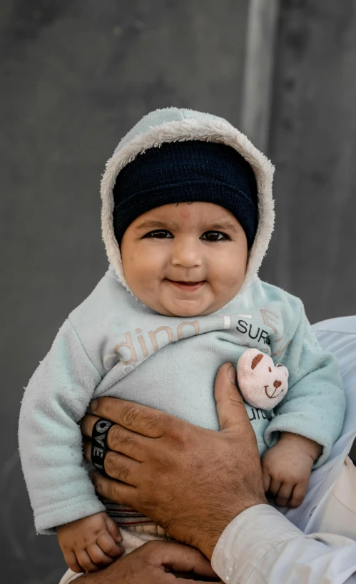 a man holding a baby in his arms, by Micha Klein, pexels contest winner, wearing beanie, smug smile, khyzyl saleem, portrait image