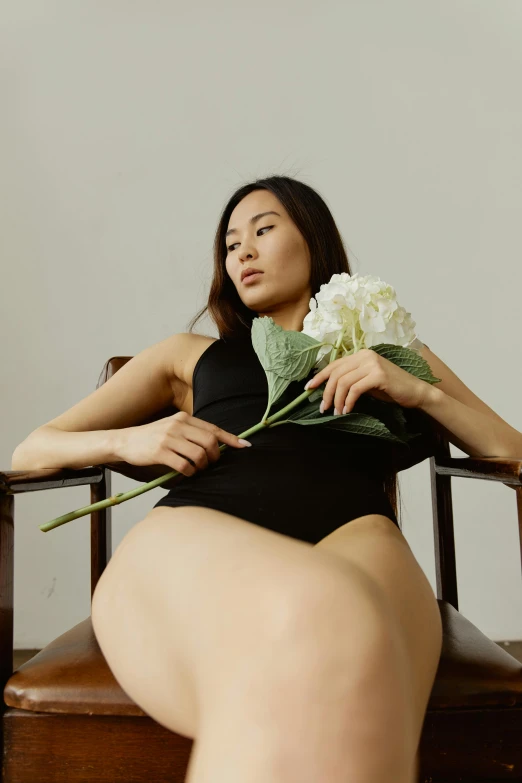 a woman sitting in a chair holding a flower, an album cover, inspired by Wang E, unsplash, black swimsuit, asian human, pose 4 of 1 6, anatomy
