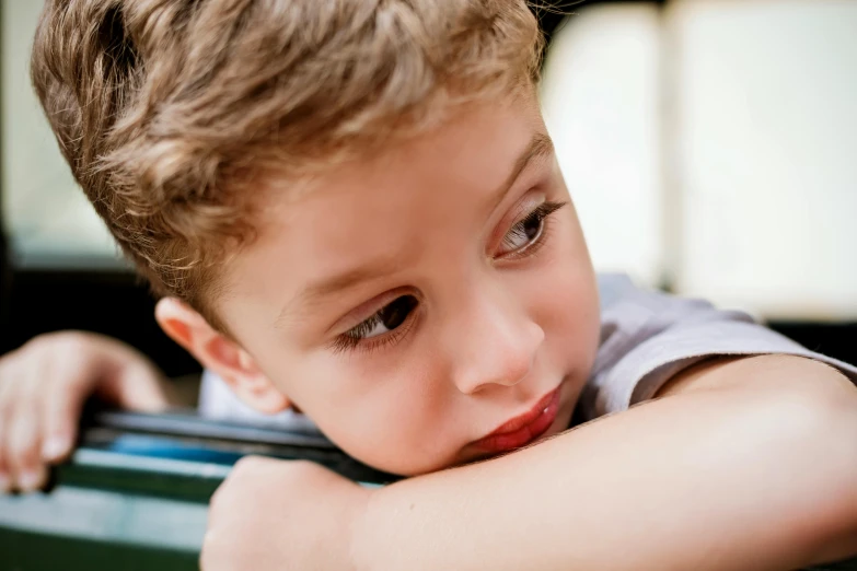 a young boy leaning on top of a green suitcase, trending on pexels, mannerism, exhausted face close up, sitting on bench, 4yr old, looking from shoulder