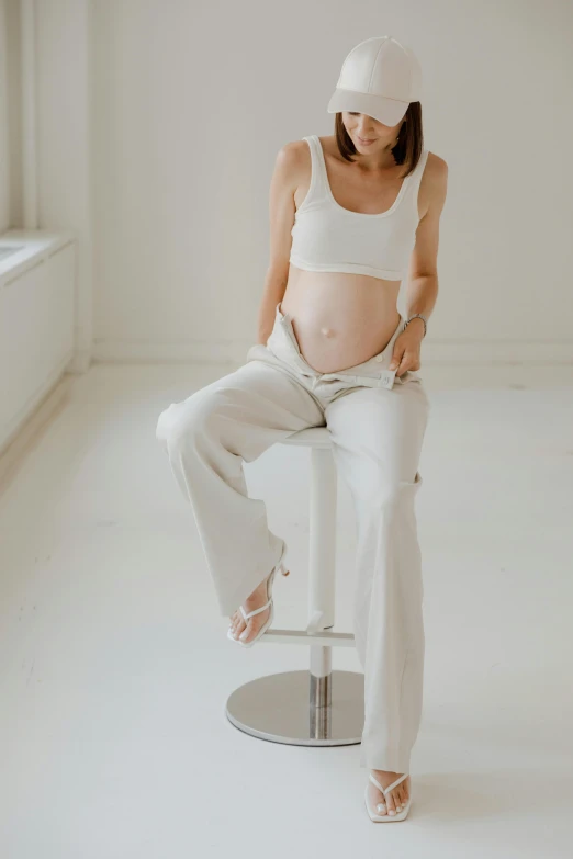 a pregnant woman sitting on a stool in a white room, by Nina Hamnett, trending on pexels, bare midriff, silver，ivory, gif, maternal