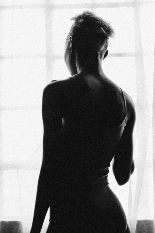 a black and white photo of a woman standing in front of a window, inspired by Lillian Bassman, flickr, beautiful female body silhouette, black girl, :: morning, with his back turned