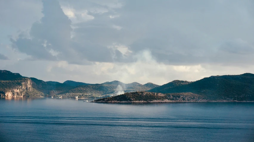 a large body of water with mountains in the background, by Exekias, pexels contest winner, happening, smoke from chimneys, croatian coastline, slide show, light haze
