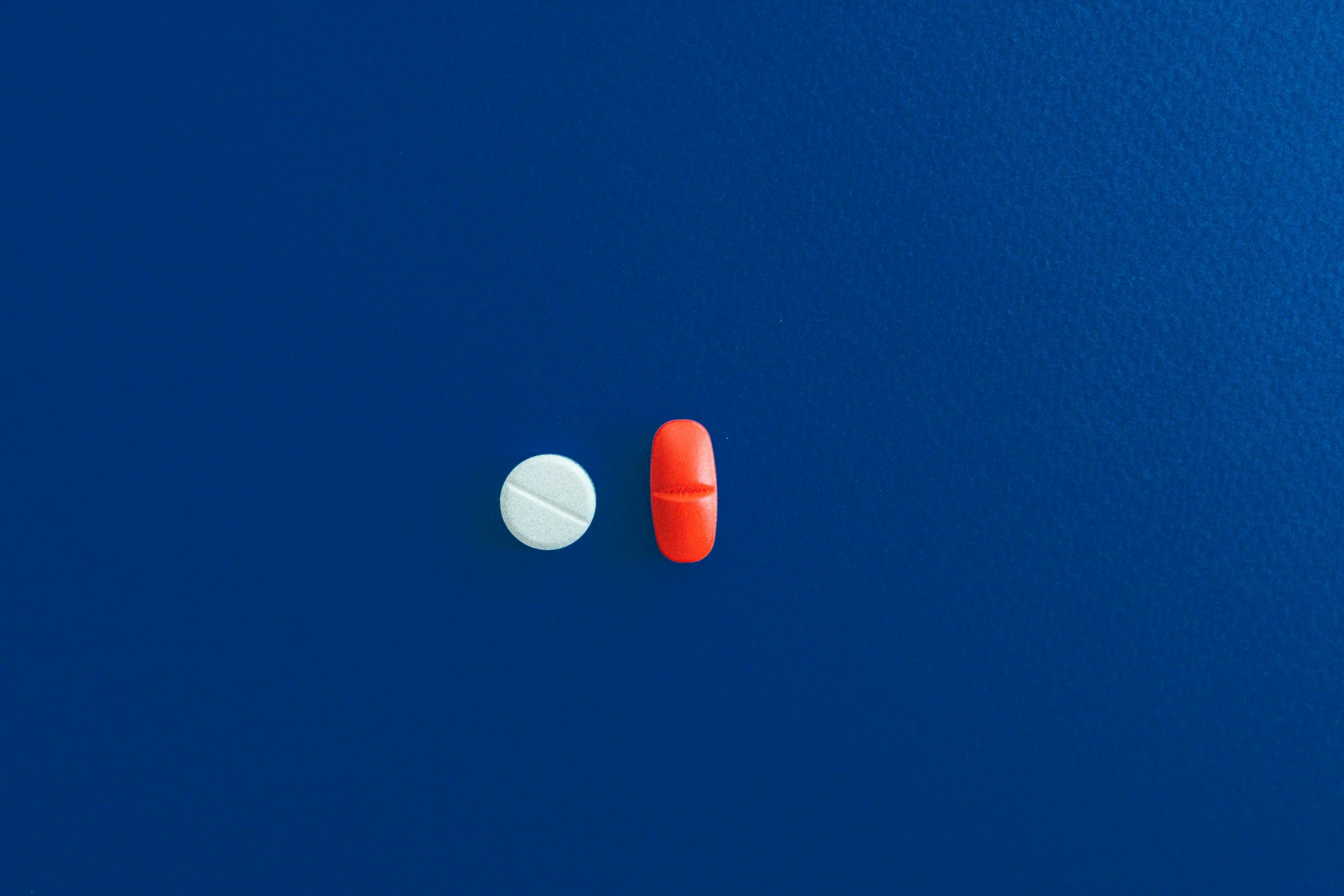 two pills sitting next to each other on a blue surface, by Julian Allen, plasticien, boats, white and orange, one is red, a high angle shot