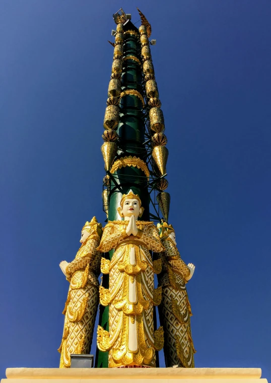 a golden statue in front of a blue sky, by Dan Content, cloisonnism, very long spires, wearing elaborate green and gold, stacked image, myanmar