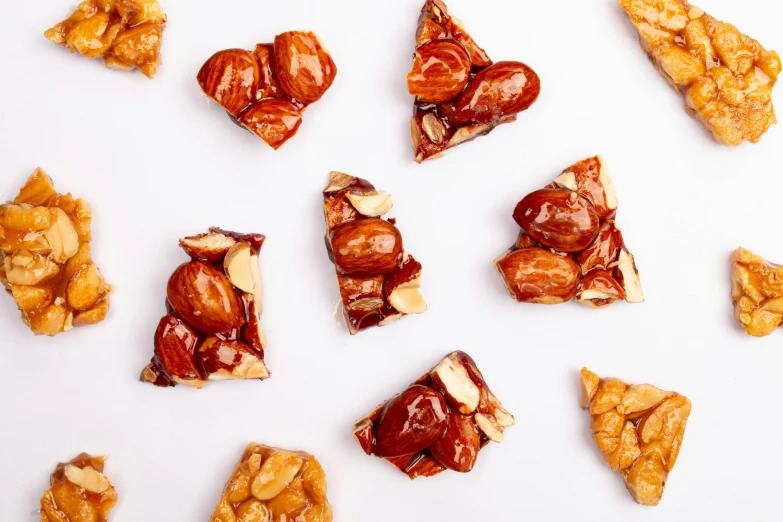 a number of pieces of food on a white surface, by Nicolette Macnamara, trending on pexels, hurufiyya, brittle. highly detailed, caramel, nut, high quality product image”